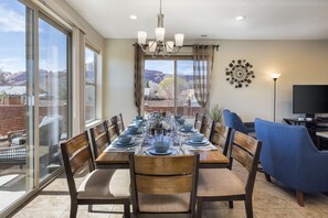 A dining area with a large table set for six, surrounded by chairs, a chandelier, and a TV on a stand. - New Listing Discounts | Private Spa | Bikes | Pool | Garage | DT Location | 673 (Moab)
