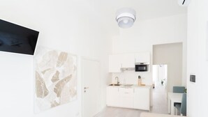 A modern hotel room with a bed, a small kitchenette, a flat-screen TV, and a wall-mounted artwork. - Gioberti Apartment 202 (ROMA)