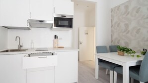 A modern kitchen with white cabinetry, a built-in microwave, and a sink. There is a dining area with a white table and blue chairs. - Gioberti Apartment 202 (ROMA)