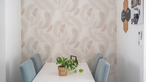 A dining area with a white table, two blue chairs, a woven basket with a plant, and a patterned wallpaper. - Gioberti Apartment 202 (ROMA)