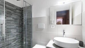 Ein modernes Badezimmer mit einer gläsernen Duschkabine, einem weißen Waschbecken und einer Toilette.