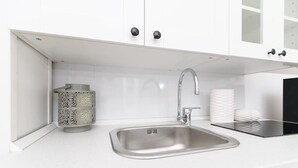 Une cuisine moderne dotée d’un évier en acier inoxydable, de meubles blancs et d’un récipient décoratif en métal.