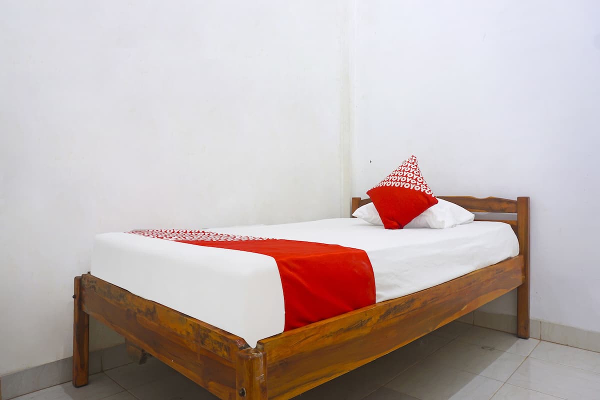 Un simple lit en bois, recouvert d’une couette blanche et rouge, avec un oreiller rouge et un oreiller blanc orné d’un motif rouge.