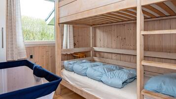 A bunk bed room with a window, wooden walls, and a small table.