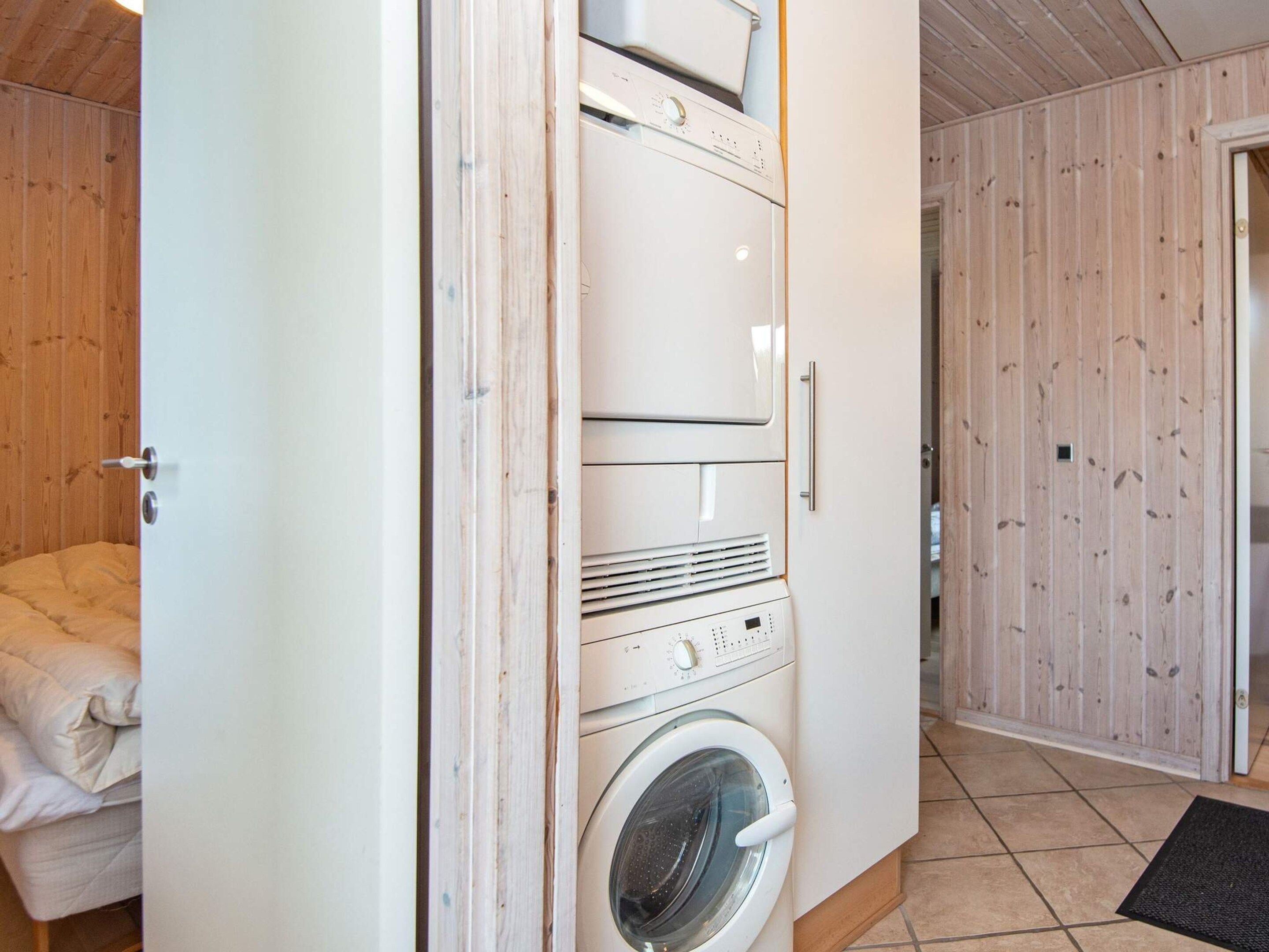 A laundry room with stacked washing machines and dryers, wooden walls, and a bed with a white duvet.