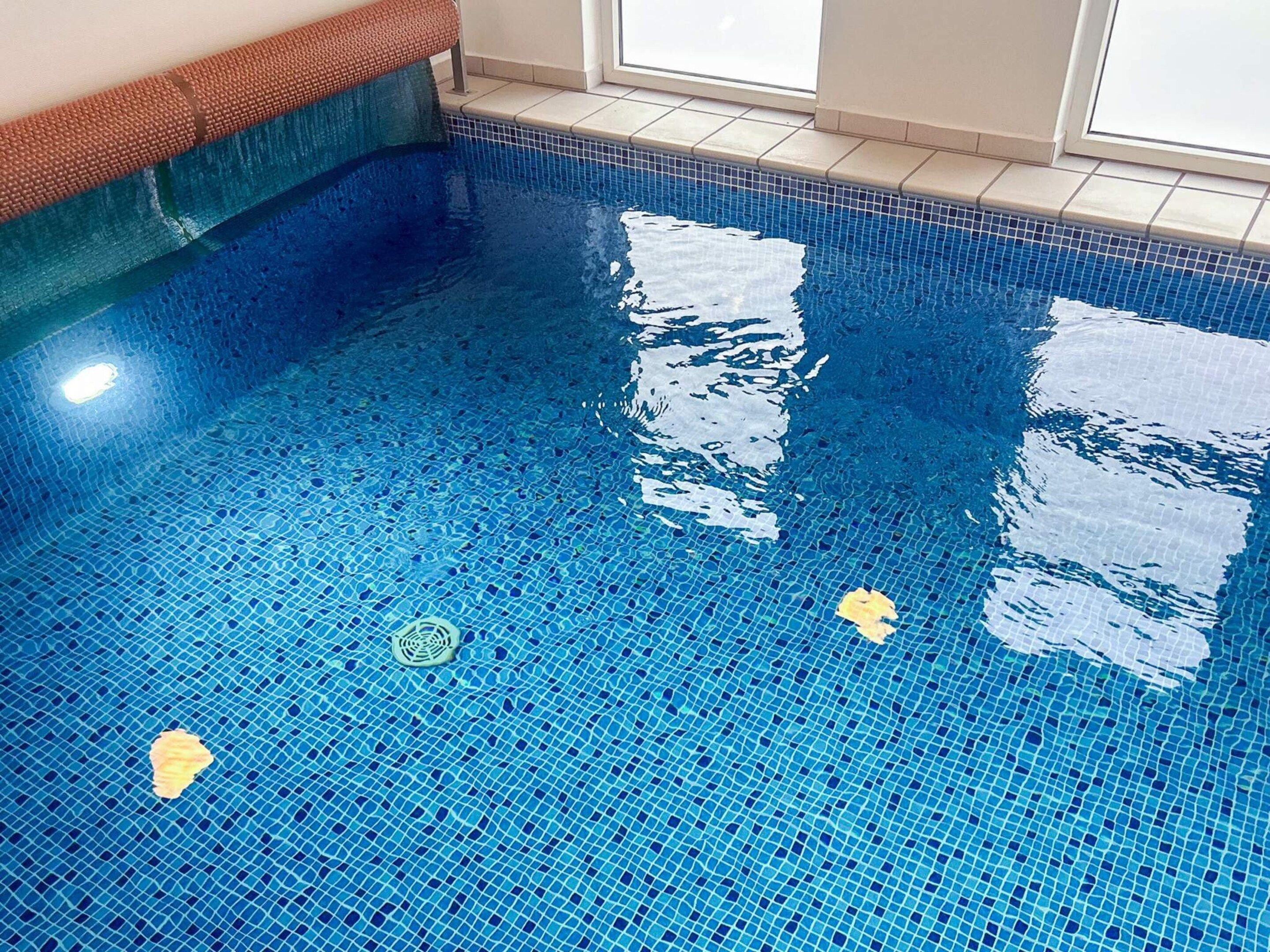 A clear indoor swimming pool with blue mosaic tiles and a drain in the center.
