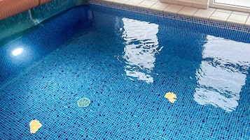 A clear indoor swimming pool with blue mosaic tiles and a drain in the center.