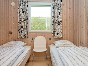 A room with two single beds, a white chair, wooden walls, a window with curtains, and a view of greenery outside. - 5 Star Holiday Home in Hejls (Hejls)