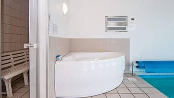 A bathroom with a white bathtub, a bench, a blue towel, and a tiled floor.