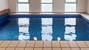 Une piscine à l’eau d’un bleu cristallin, entourée d’une terrasse carrelée et dotée de grandes fenêtres aux vitres dépolies.