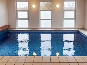 A swimming pool with clear blue water, surrounded by a tiled deck and large windows with frosted glass panes. - 5 Star Holiday Home in Hejls (Hejls)