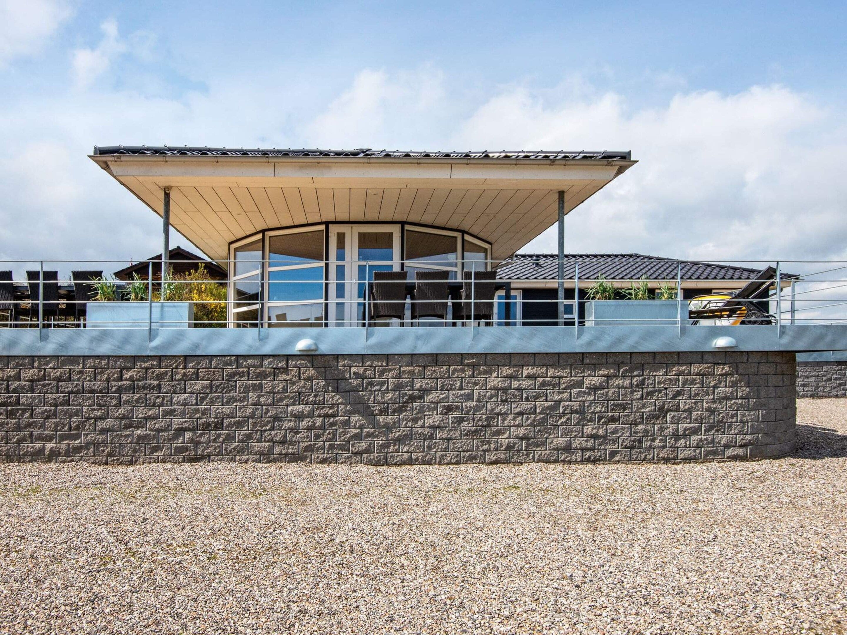 A modern building with a covered patio area, a stone wall, and a gravel ground.