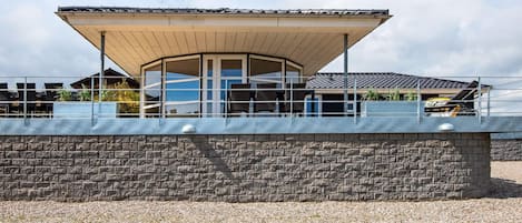 A modern building with a covered patio area, a stone wall, and a gravel ground.