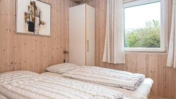 A room with two beds, a wardrobe, a window with curtains, and a framed picture on the wall.