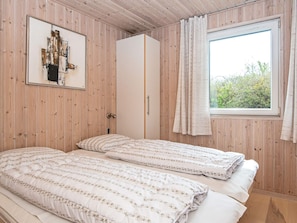 A room with two beds, a wardrobe, a window with curtains, and a framed picture on the wall.