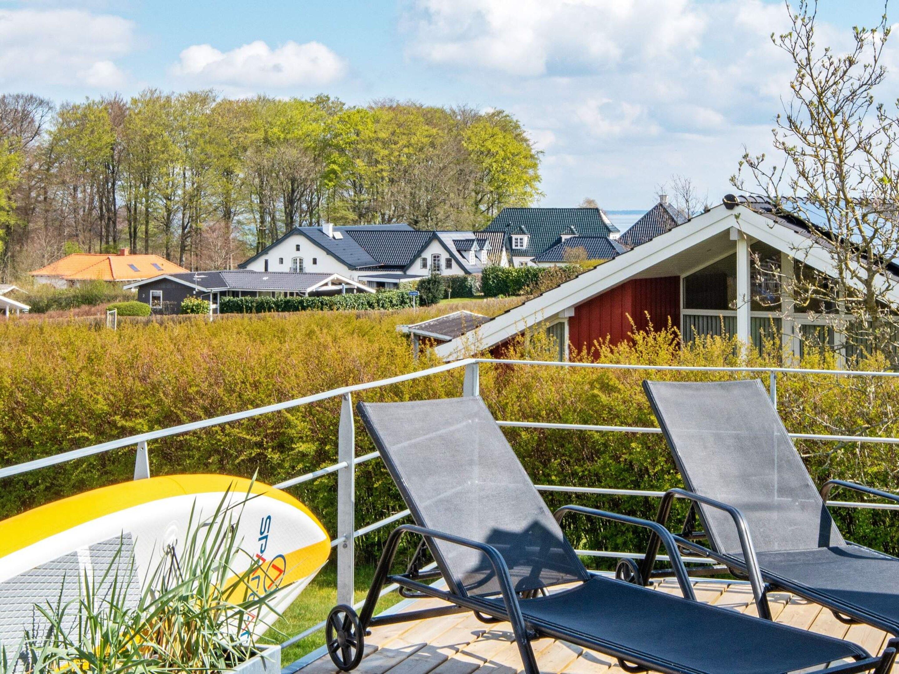 A poolside area with lounge chairs and a surfboard, surrounded by houses and greenery.