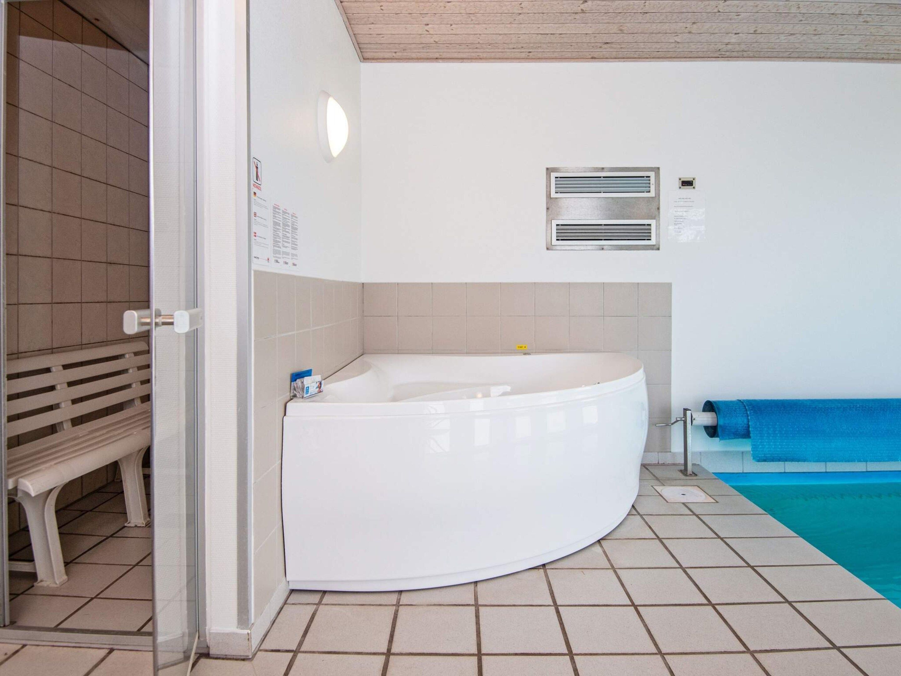 A bathroom with a white bathtub, a bench, a blue towel, and a tiled floor.