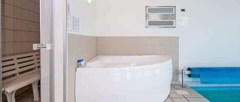 A bathroom with a white bathtub, a bench, a blue towel, and a tiled floor.