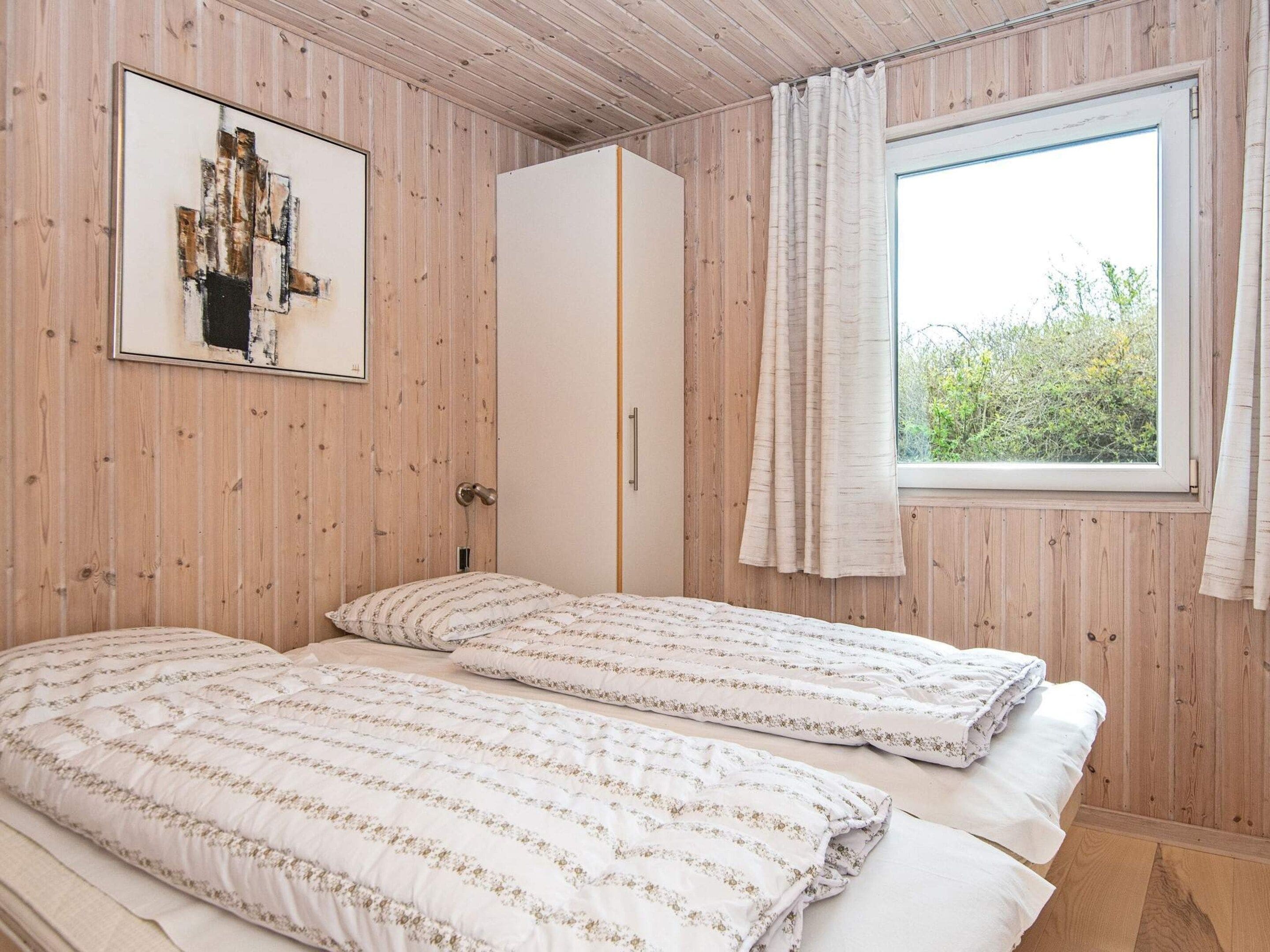 A room with two beds, a wardrobe, a window with curtains, and a framed picture on the wall.
