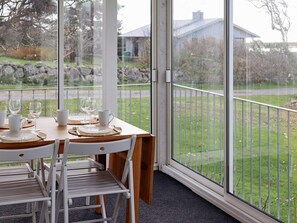 Een eetgedeelte met een tafel voor vier personen, stoelen en uitzicht op een gazon door grote ramen.