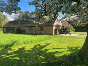 A small brick building with a sloped roof, a wooden door, and a picnic table in the yard. - Light and airy stylish barn conversion set in peaceful countryside. (Henley in arden)