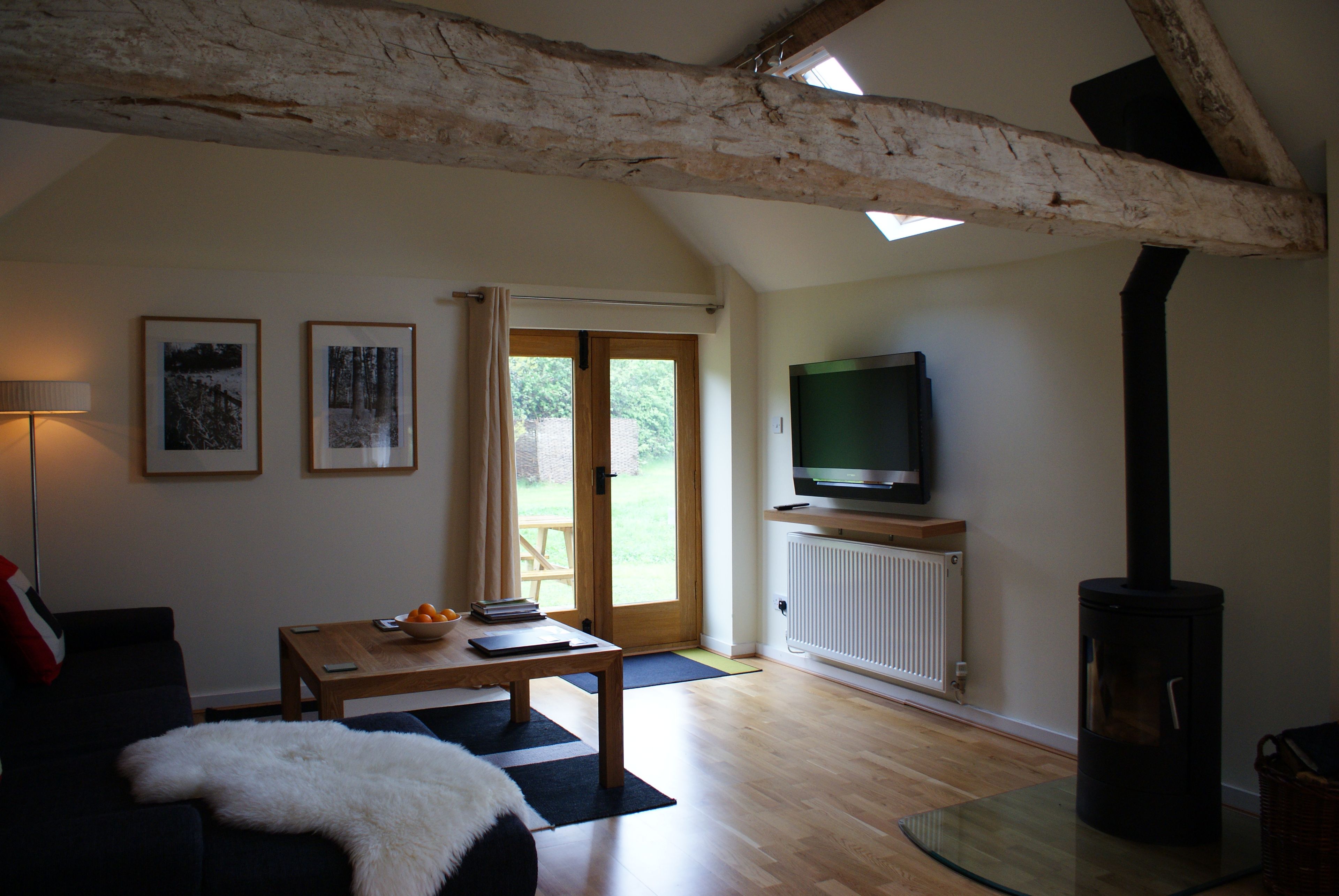 A living room with a wooden ceiling, a television on a stand, a sofa, a table with books and a bowl, and a door leading outside.