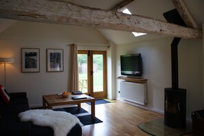 A living room with a wooden ceiling, a television on a stand, a sofa, a table with books and a bowl, and a door leading outside.