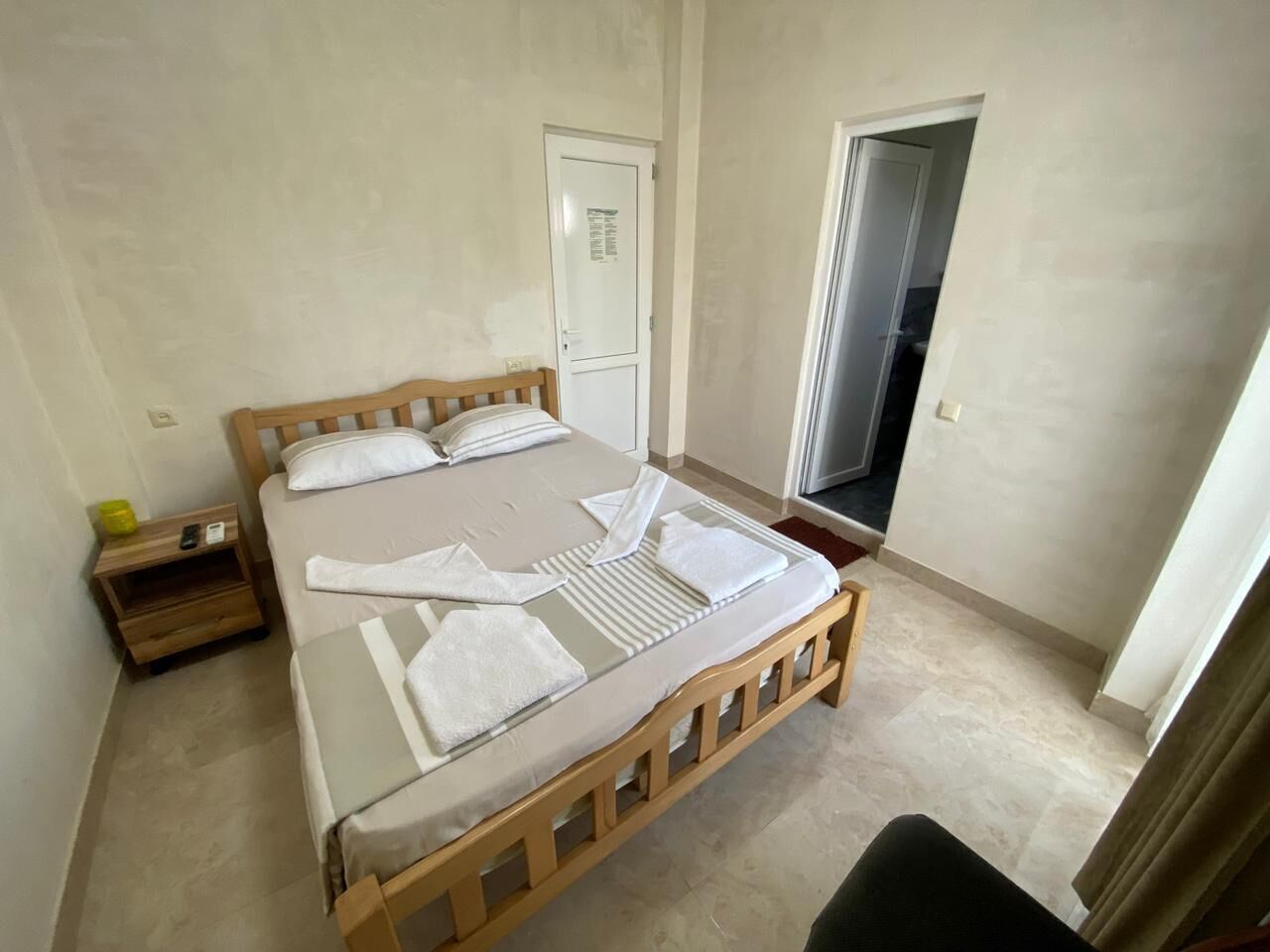 A bedroom with a wooden bed, a nightstand, a door, and a small window.