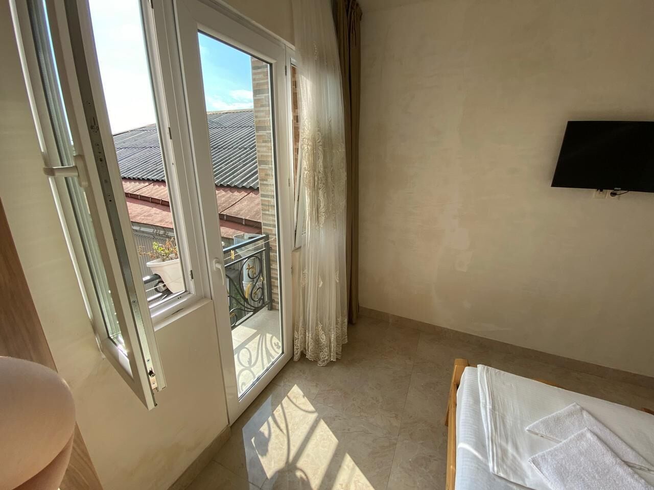 A room with a sliding glass door leading to a balcony, a bed with a white cover, and a mounted TV on the wall.