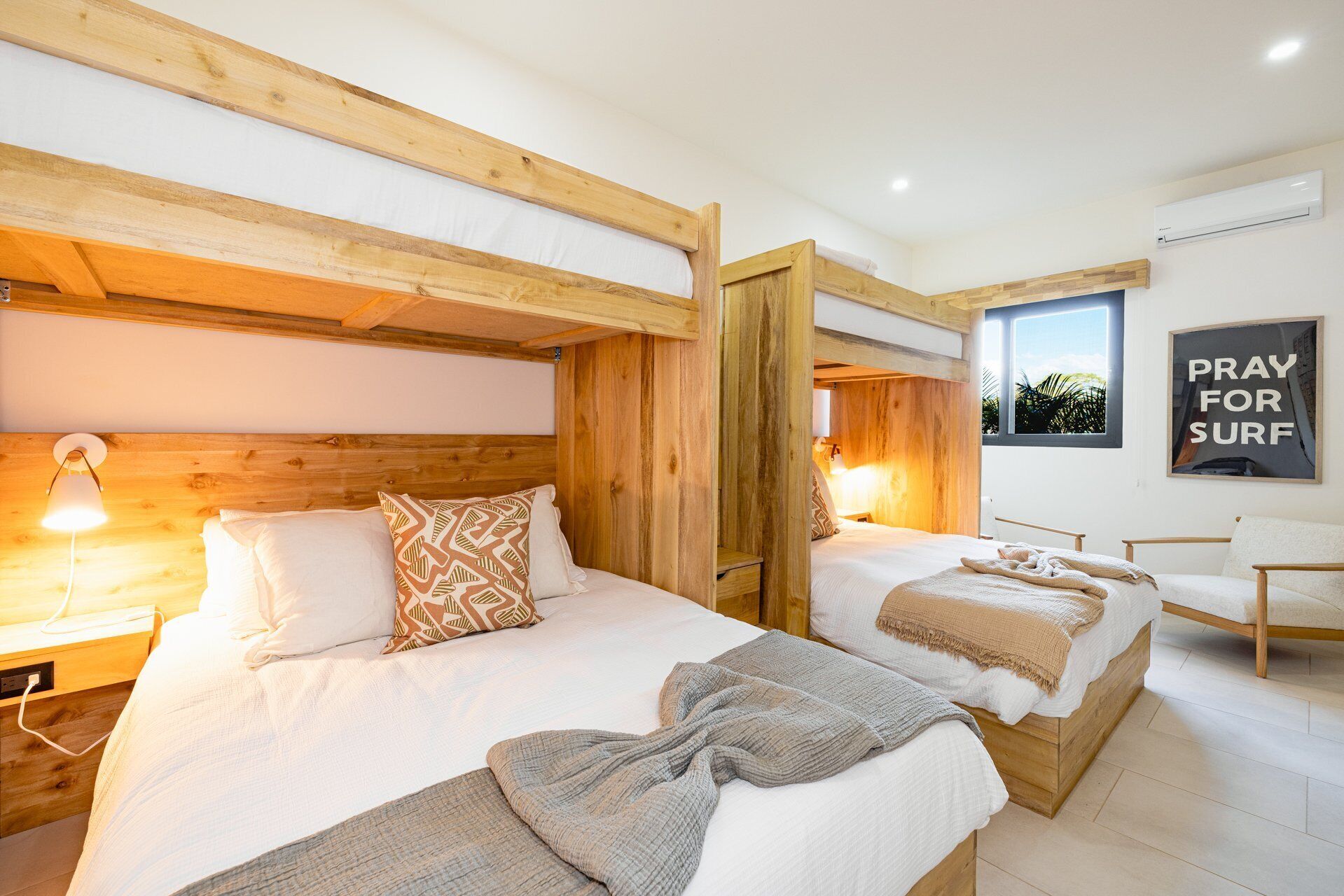 Ein Hotelzimmer mit zwei Betten, Holz-Kopfteilen, einem großen Fenster und einem Schild mit der Aufschrift 'PRAY FOR SURF'.
