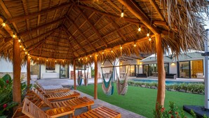 A covered outdoor seating area with wooden loungers and hanging hammocks, a pool, and a well-maintained lawn. - 5 Min Drive to the Beach, Private Heated Jacuzzi - Sleeps 20 (Playa Avellana)