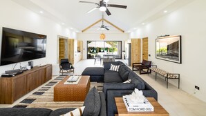A spacious living room with a large flat-screen TV, a dark-colored sofa, a wooden coffee table, and a ceiling fan. - 5 Min Drive to the Beach, Private Heated Jacuzzi - Sleeps 20 (Playa Avellana)