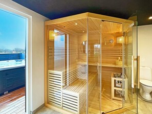 A modern bathroom with a glass enclosure, wooden slats, a built-in toilet, and a small shelf with toiletries. - 14 Person Holiday Home in Vaeggerlose (Vaeggerlose)