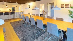 A modern dining area with a long wooden table, grey chairs, pendant lighting, and a vase with flowers. - 14 Person Holiday Home in Vaeggerlose (Vaeggerlose)