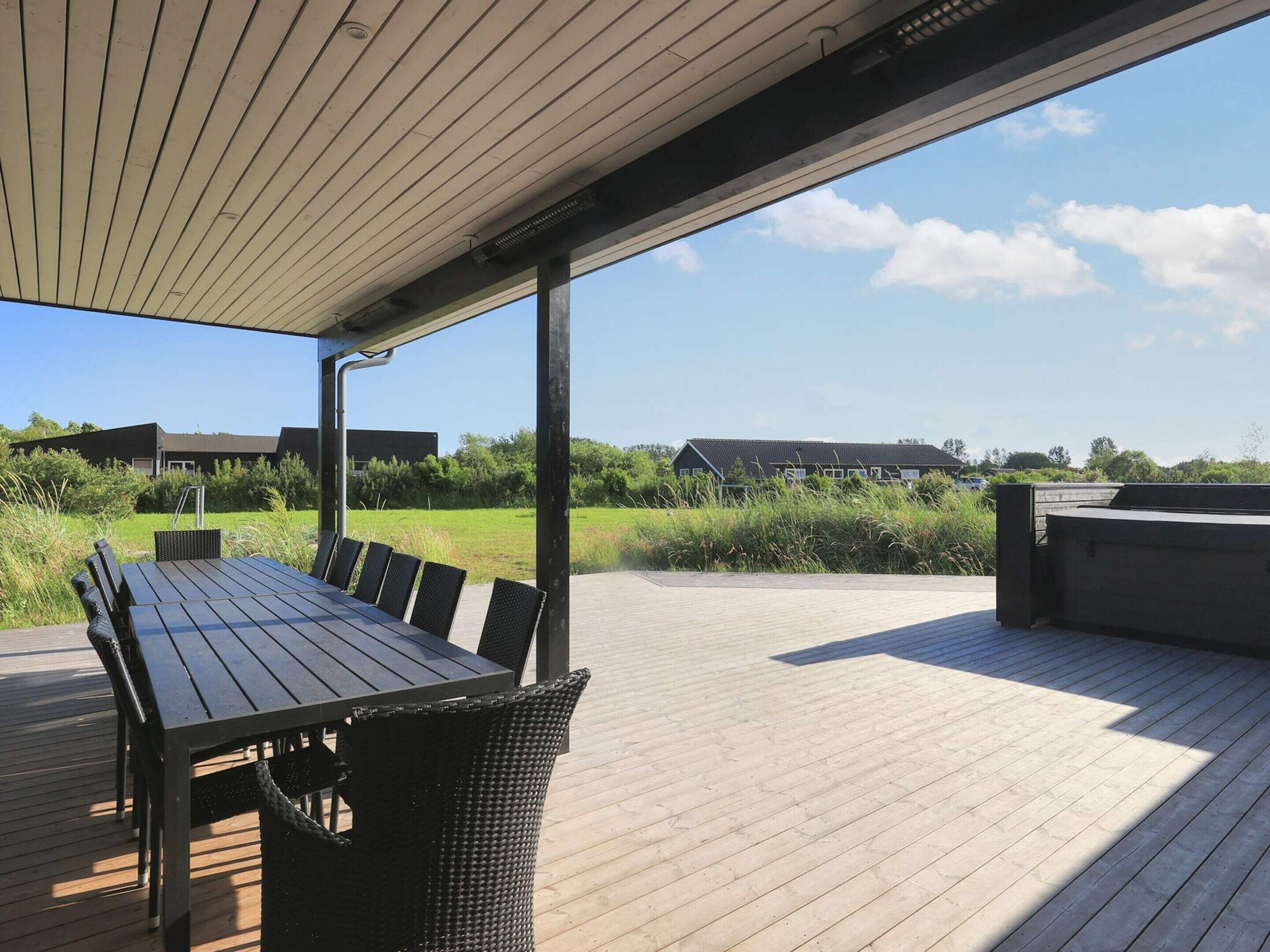 An outdoor patio with a wooden table and chairs, a covered area, and a view of buildings and greenery in the background.