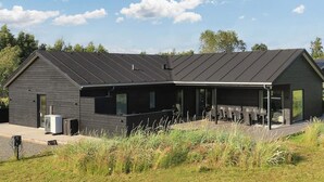 A modern building with a sloped roof, a covered outdoor seating area, and a grassy foreground. - 14 Person Holiday Home in Vaeggerlose (Vaeggerlose)