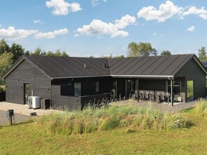 A modern building with a sloped roof, a covered outdoor seating area, and a grassy foreground. - 14 Person Holiday Home in Vaeggerlose (Vaeggerlose)