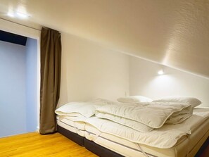 A single bed with white bedding in a room with light-colored walls and a wooden floor.