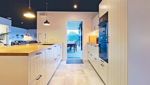 A modern kitchen with white cabinetry, a wooden countertop, and a view into a dining area. - 14 Person Holiday Home in Vaeggerlose (Vaeggerlose)