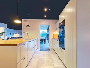 A modern kitchen with white cabinetry, a wooden countertop, and a view into a dining area. - 14 Person Holiday Home in Vaeggerlose (Vaeggerlose)
