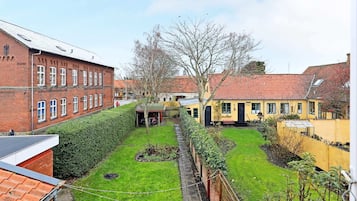 A courtyard with a green lawn, a brick building, and a yellow building with a red roof.