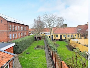 A courtyard with a green lawn, a brick building, and a yellow building with a red roof. - 3 Person Holiday Home in Aeroskobing (Aeroskobing)