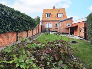 A brick house with a tiled roof, a garden with various plants, and a metal gate. - 3 Person Holiday Home in Aeroskobing (Aeroskobing)