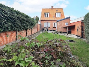 A brick house with a tiled roof, a garden with various plants, and a clear sky. - 3 Person Holiday Home in Aeroskobing (Aeroskobing)