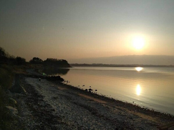 Una superficie de agua tranquila bajo un cielo despejado, con una costa lejana.