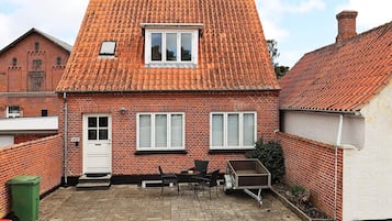 A two-story brick house with a tiled roof, a front door, and a small patio area with a table and chairs.