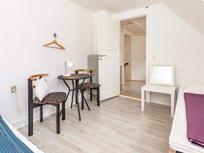 Una habitación pequeña con cama, una mesita de noche con lámpara, dos sillas y un perchero.