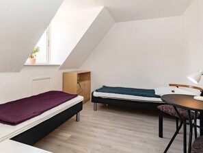 Habitación tipo dormitorio con dos camas, una mesita pequeña, una silla y una ventana con una planta.
