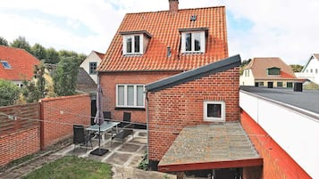 Ein zweistöckiges Backsteinhhaus mit rotem Ziegeldach, einer kleinen Terrasse mit Gartenmöbeln und einem sichtbaren Fenster.