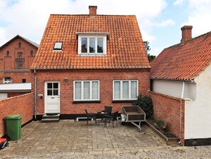 A two-story brick house with a tiled roof, a front door, and a small patio area with a table and chairs.